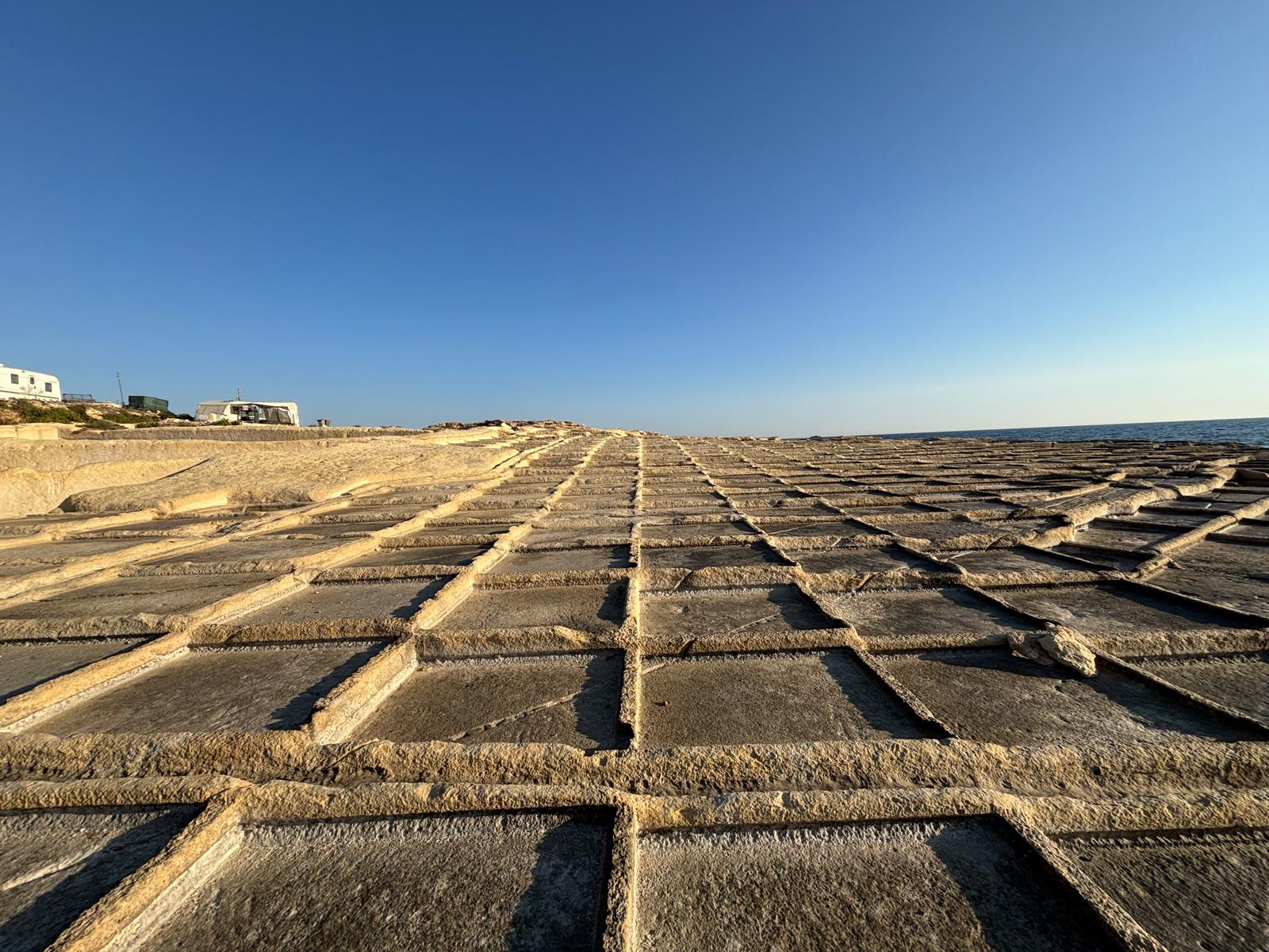 Wide expanse of the Naxxar coastal salt pan matrix looking northwest against a clear blue sky