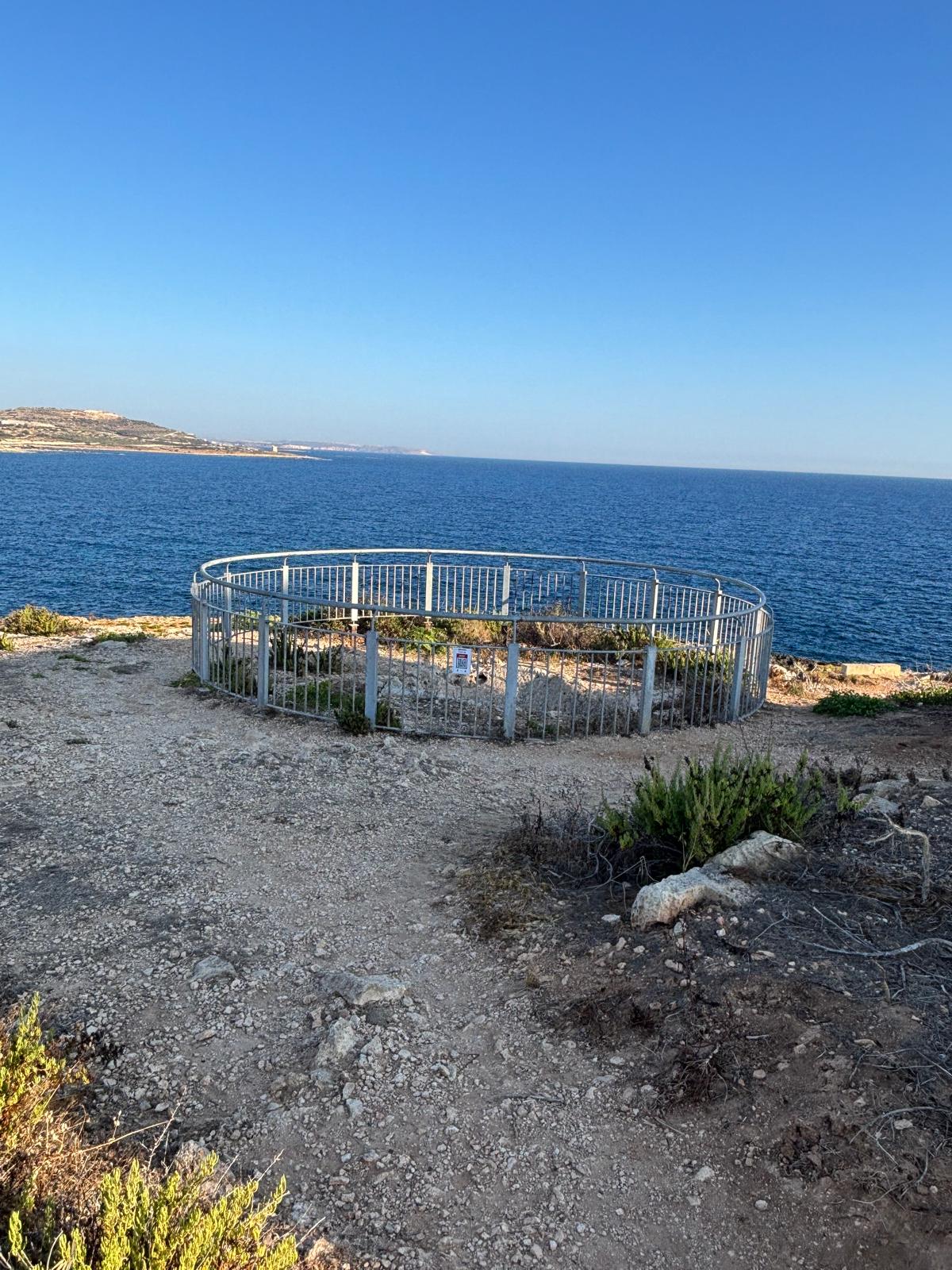 The circular safety railing encircling the Madliena Fougasse with the blue Mediterranean coastline stretching into the background