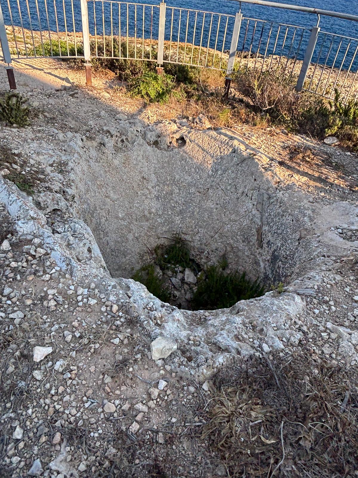 A high-angle view down into the rough rock-cut interior basin of the fougasse