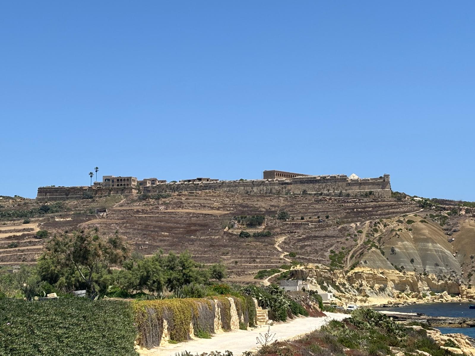 View looking inland showing the massive limestone bastions of Fort Chambray lining the high hilltop cliff edge above the valley