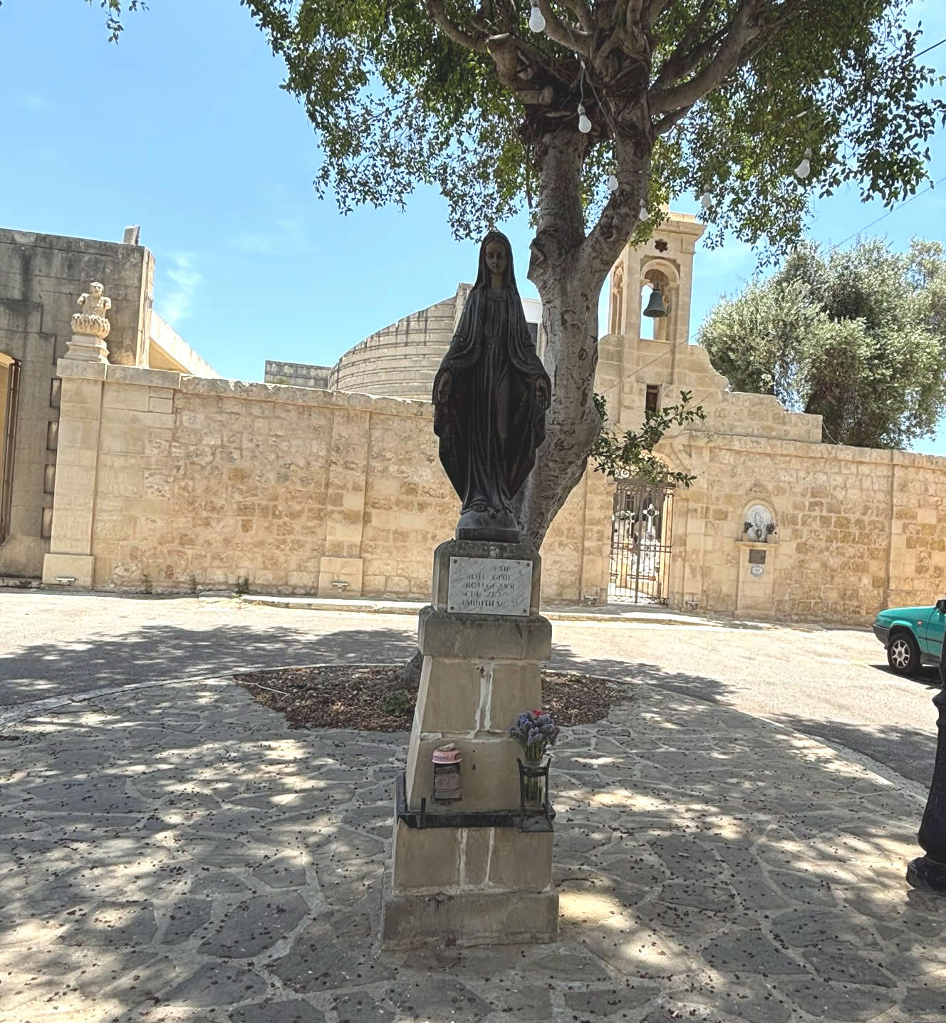 The bronze statue of the Virgin Mary standing on a limestone pedestal in the square outside Tarxien Cemetery