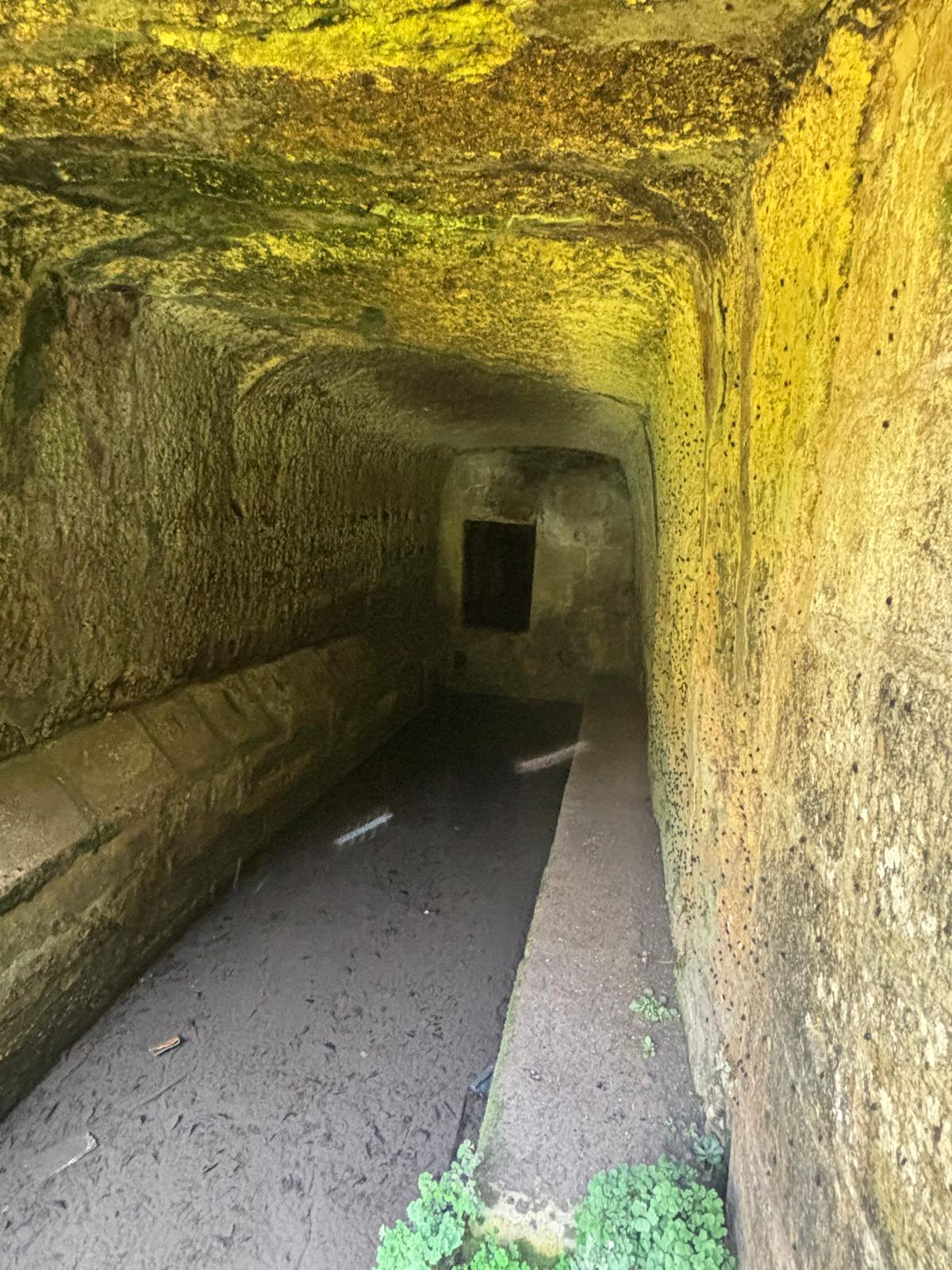 Subterranean tunnel interior of Dingli wash house showing long stone troughs and moss covered yellow rock walls