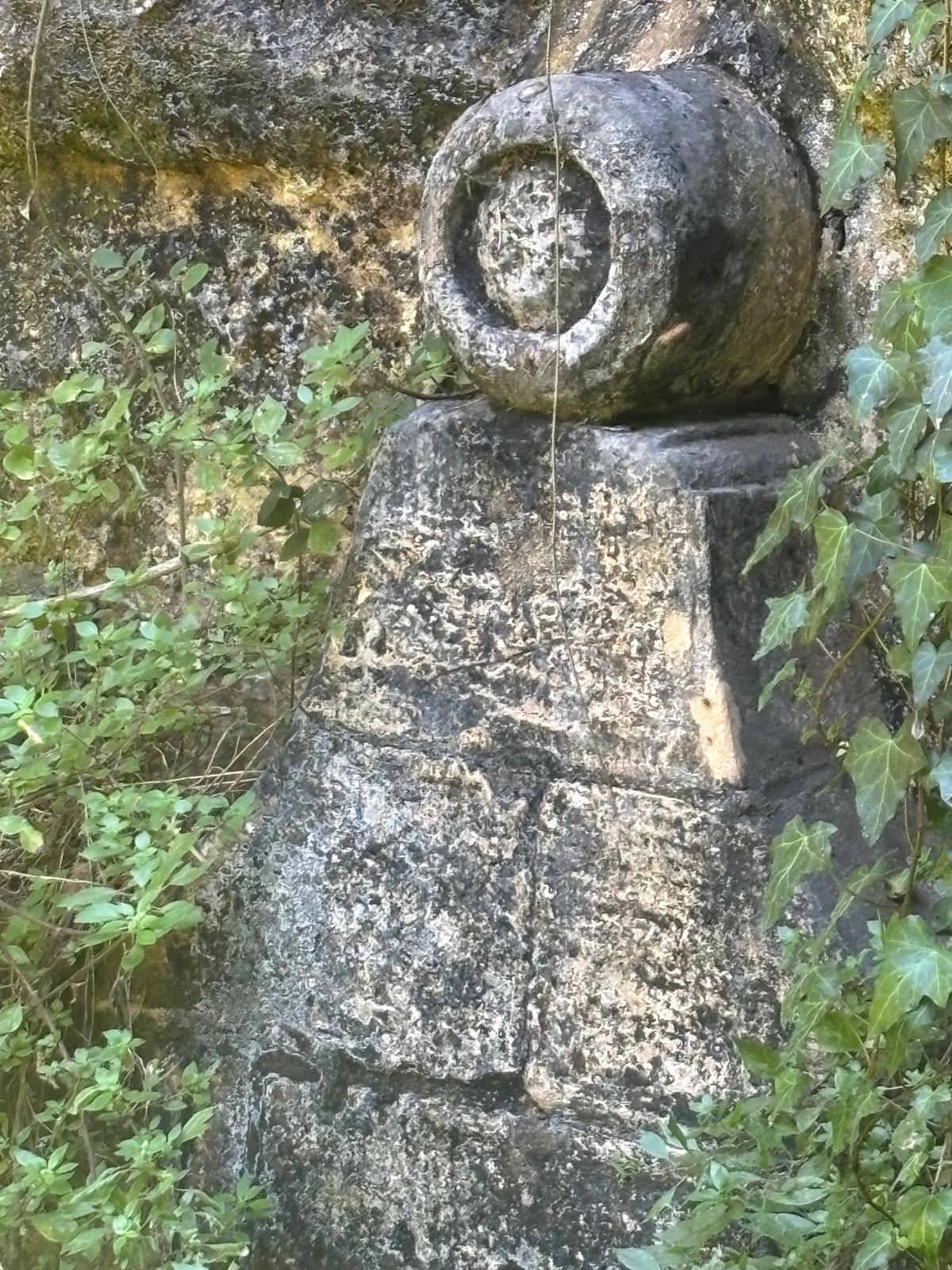A weathered cylindrical stone marker or ornament sitting on a stepped limestone pedestal outside the washhouse