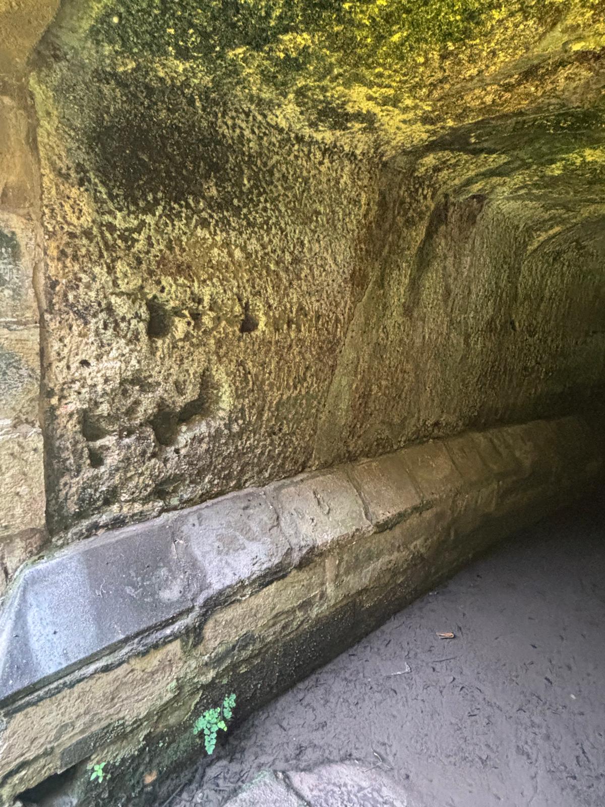 Detailed view of hand carved tool marks on the limestone wall above a continuous stone wash slab inside the vault