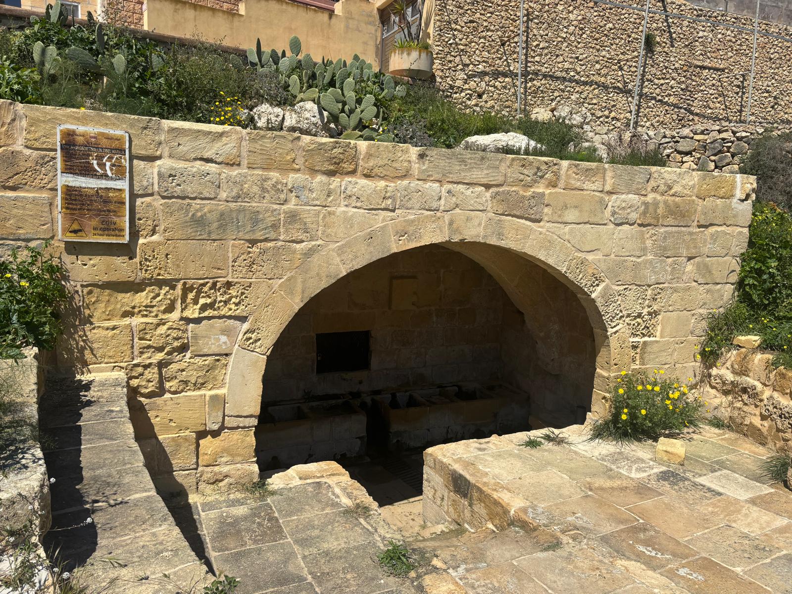Front view of the limestone barrel arch of Għajn Tuta wash house with heritage information board