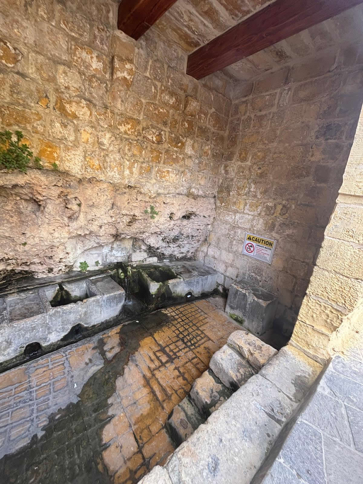Close up view of the right side stone washing basins in Ghajn ta Bendu next to a yellow caution sign