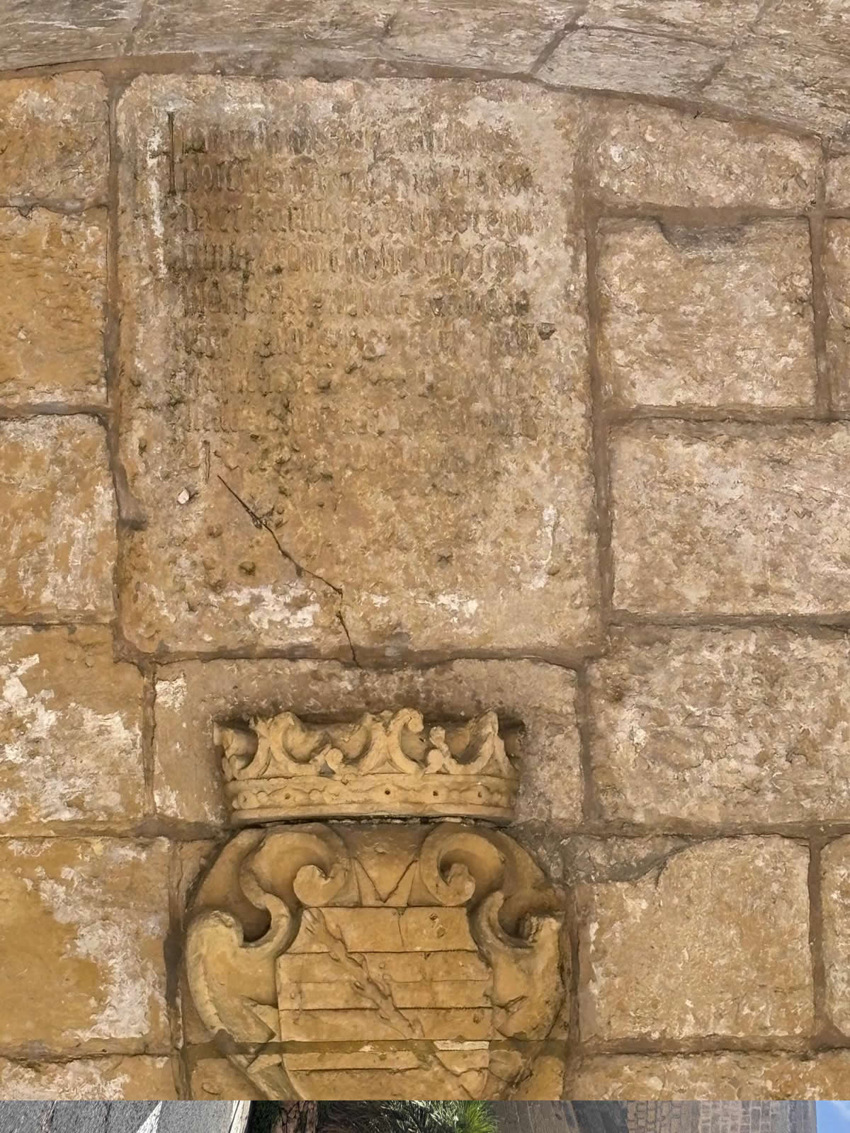 Close up detail of a carved stone armorial coat of arms topped by a crown beneath an eroded Latin inscription slab