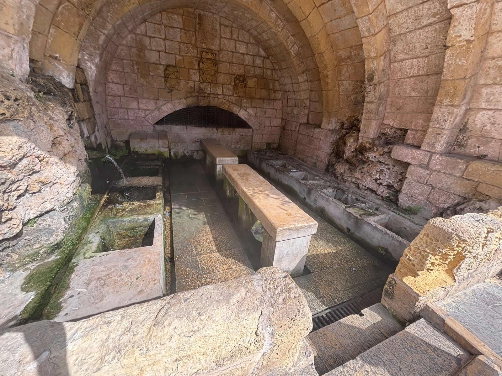 Interior wide view of the vaulted stone public wash house showing stone troughs benches and active spring water source