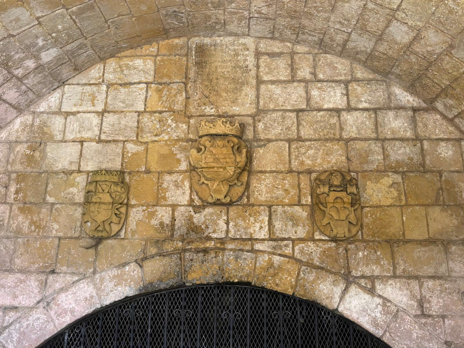 Three carved stone armorial crests of the Knights of St John mounted on the back masonry wall of the wash house
