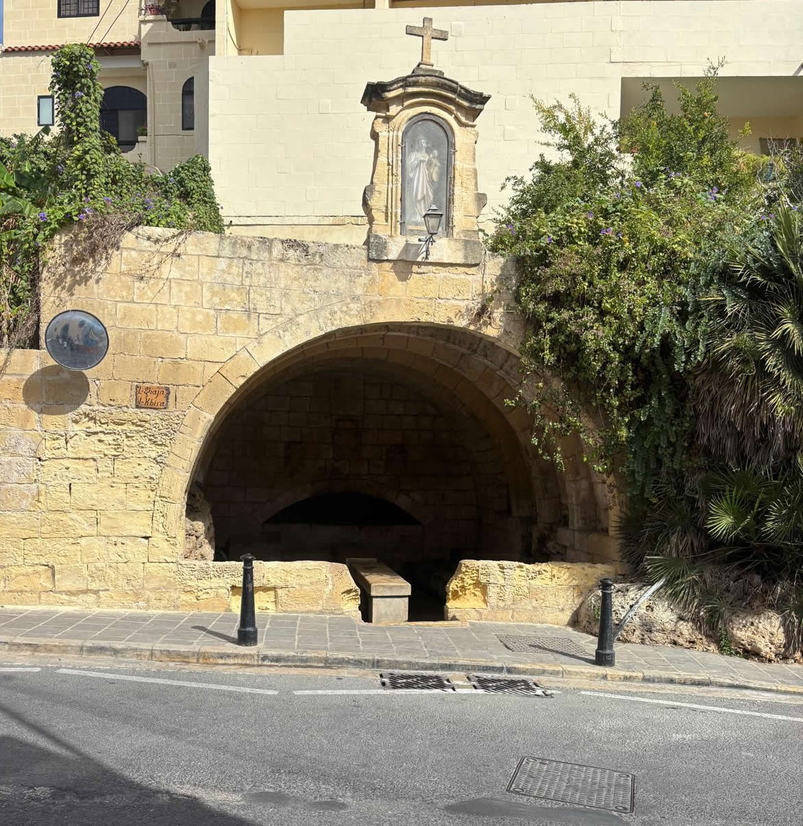 Exterior frontal view of the Fontana Knights wash house arch surrounded by green trees and roadside pavement