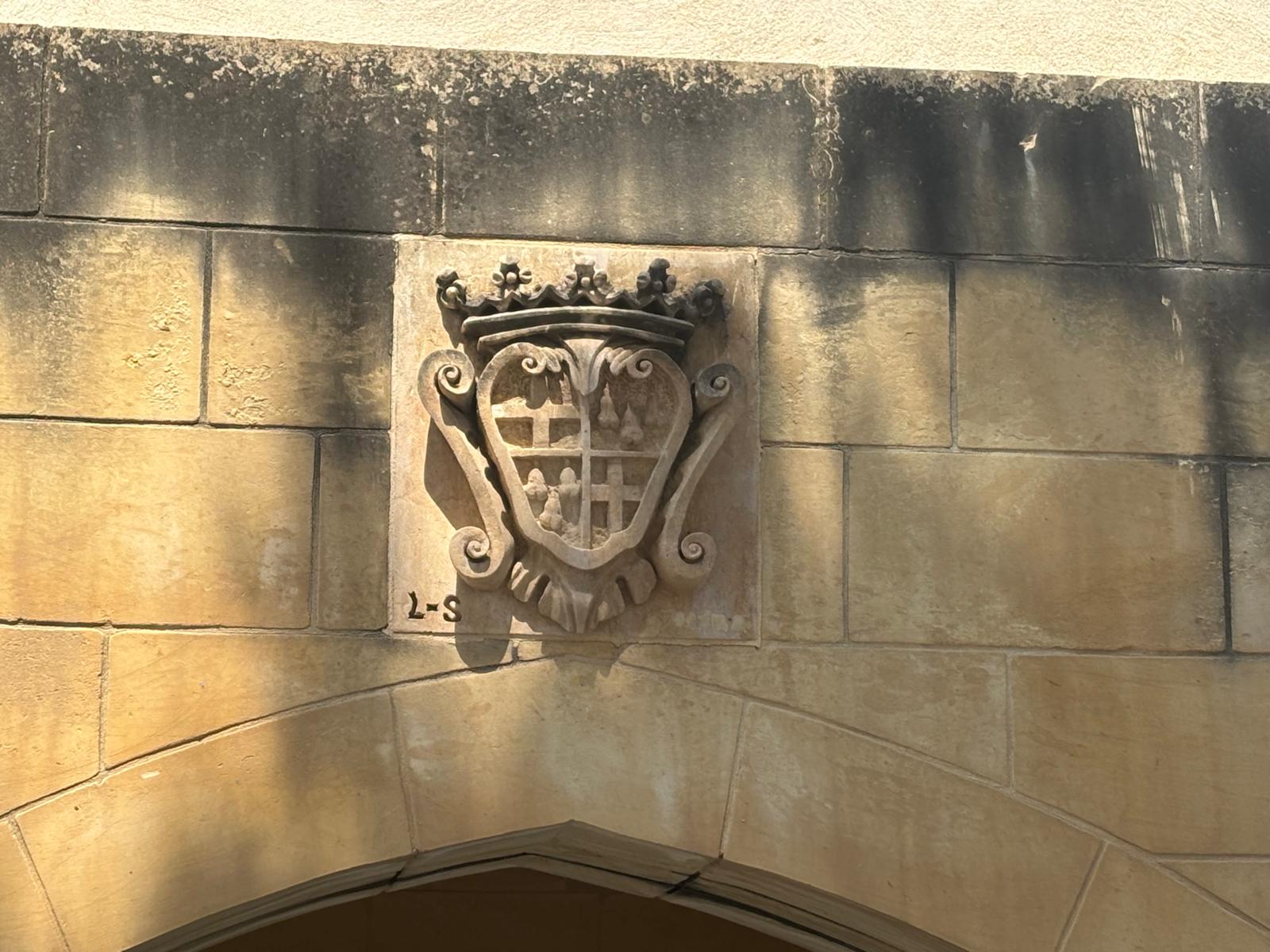 Close up of a carved stone heraldic coat of arms topped with a crown, located above the central arch
