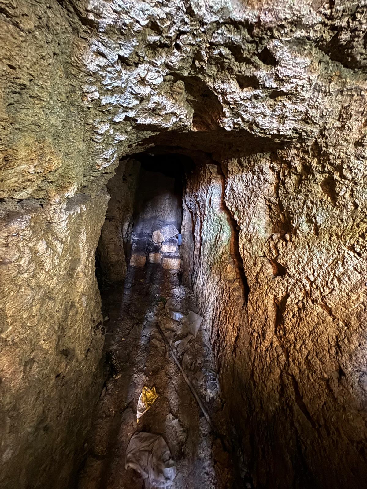 Looking into a dark, rough-hewn stone tunnel that serves as the natural water source for the wash house