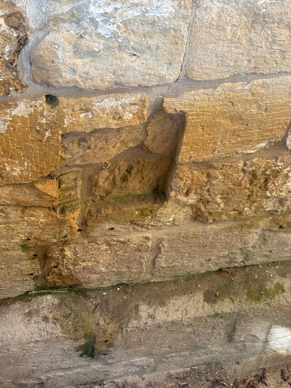 Close up of weathered, textured limestone blocks with a rectangular indentation showing tool marks or historical wear