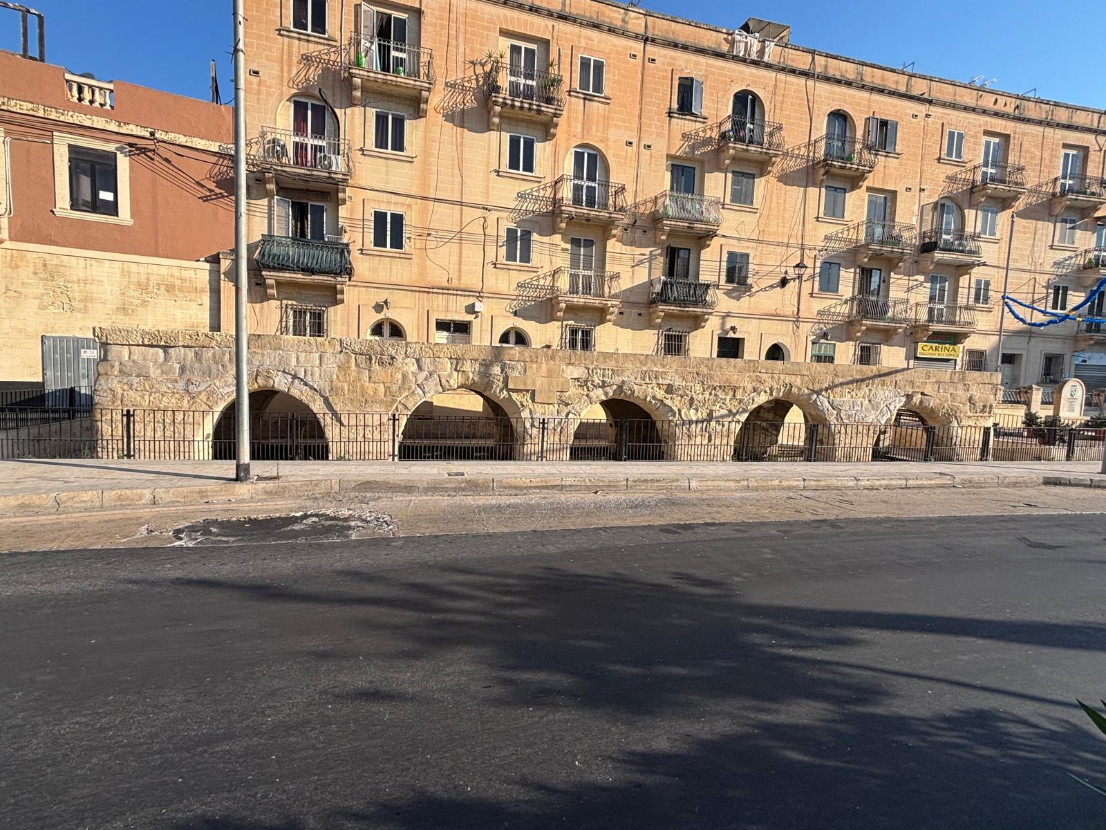 The historic low stone arch wash house structure sitting at the base of multi story modern apartment flats on Valley Road Msida