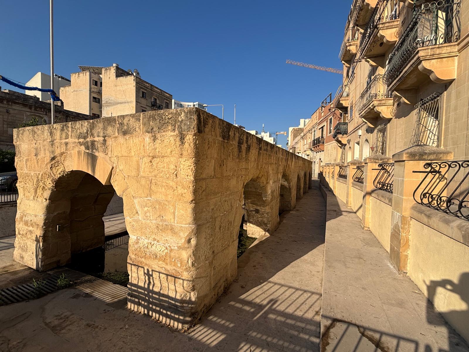 Side profile look down the long flat roof and thick stone columns of the Msida public wash house arcade