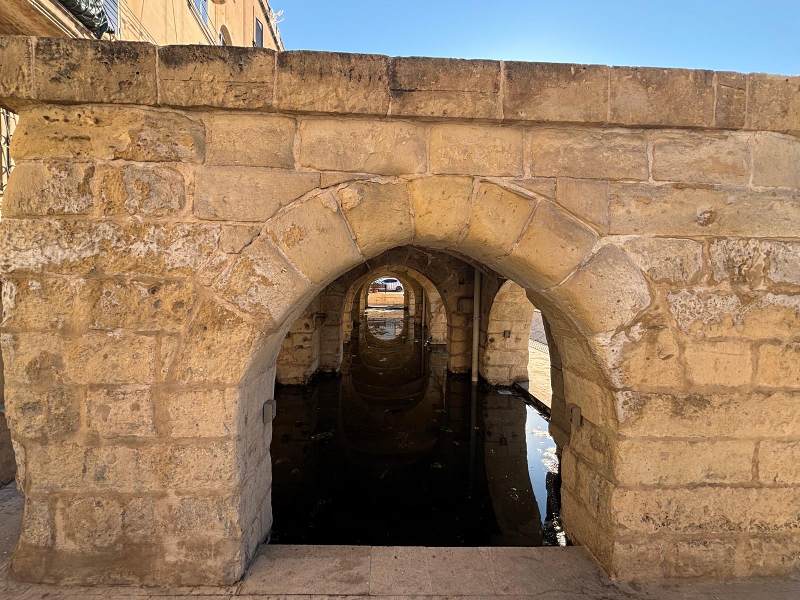 Concentric view through the inside of the Msida wash house showing arches reflecting perfectly in a pool of clear standing spring water