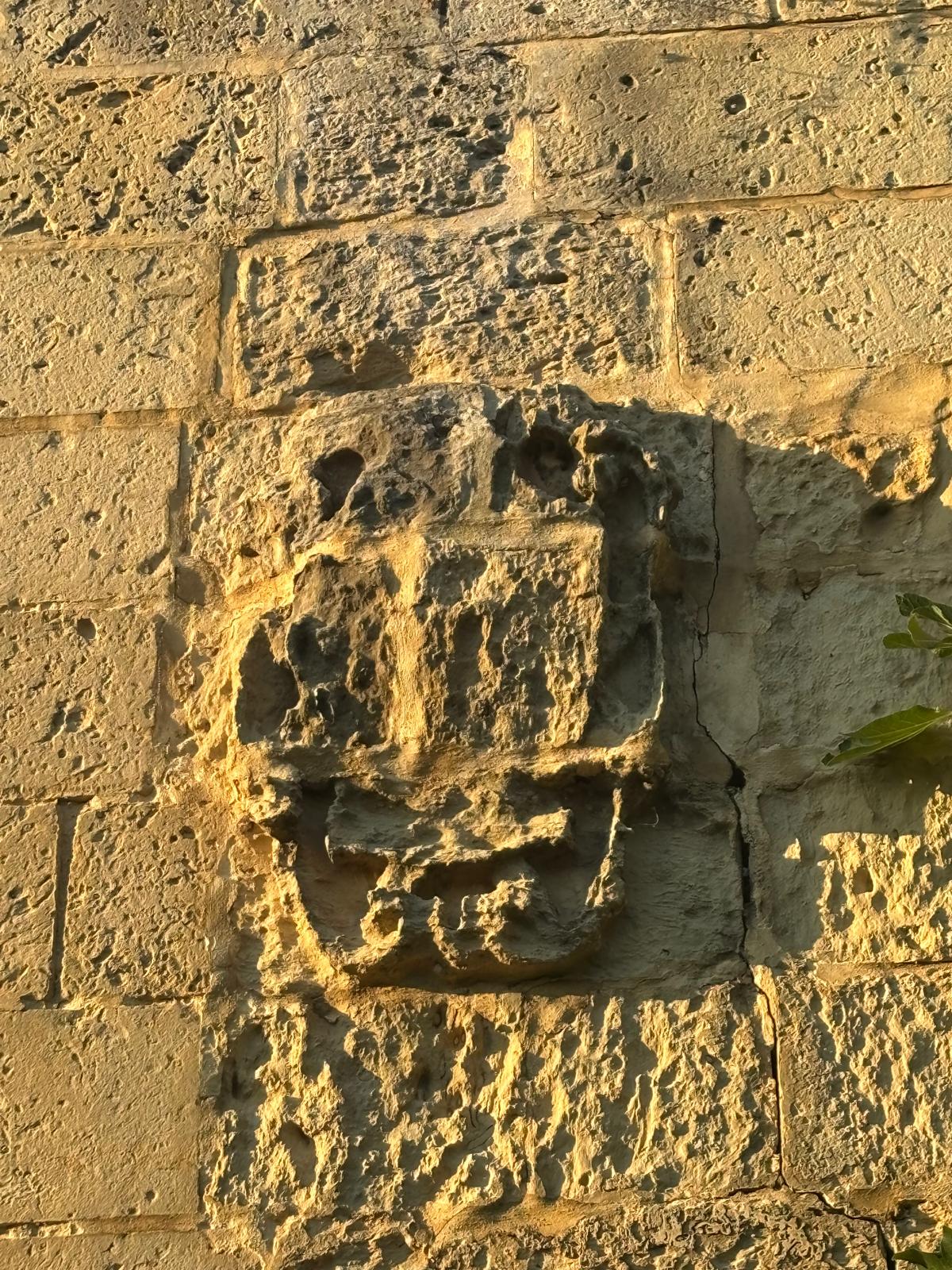 Close up of a weathered stone coat of arms carved into the limestone facade of Ghajn Hammiem