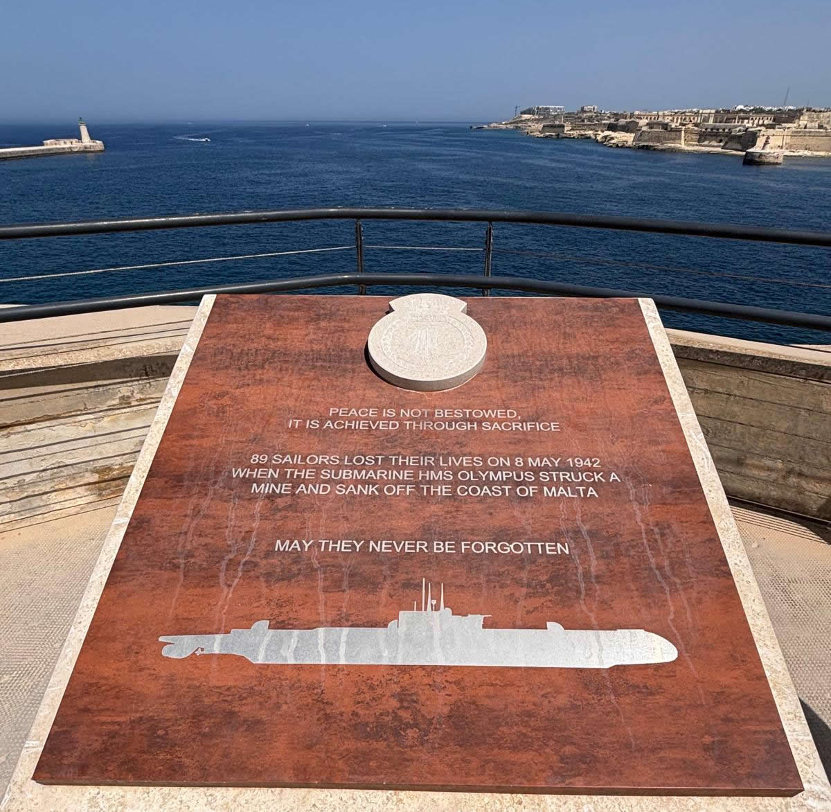 Top face inscription of the HMS Olympus memorial in Valletta, showing the submarine silhouette against the Mediterranean sea