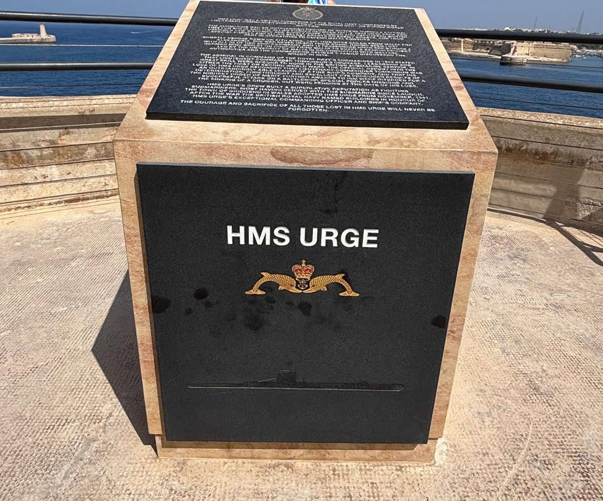 The front face of the HMS Urge stone memorial in Valletta, featuring the submarine silhouette and dolphin emblem badge.